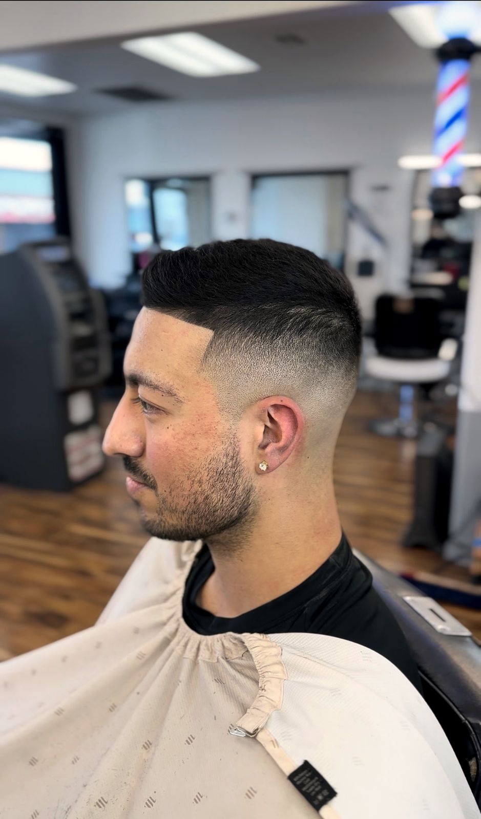 Crisp mid fade with a sharp lineup, barber pole in the background